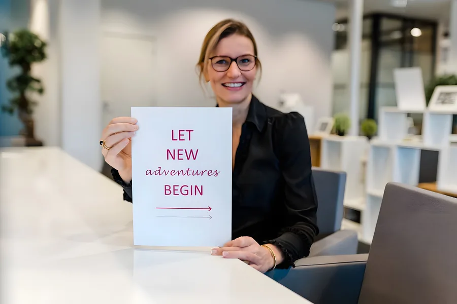 Anouk aan een witte balie met een bordje: Let new adventures begin